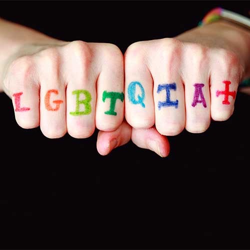 Fäuste, auf deren Finger in bunten Buschstaben steht: LGBTQIA+
