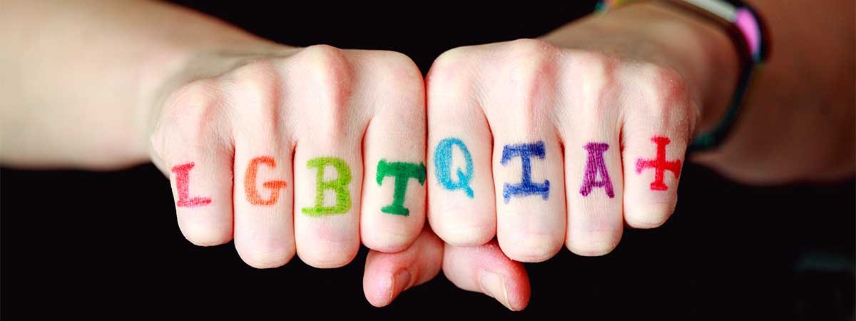 Fäuste, auf deren Finger in bunten Buschstaben steht: LGBTQIA+