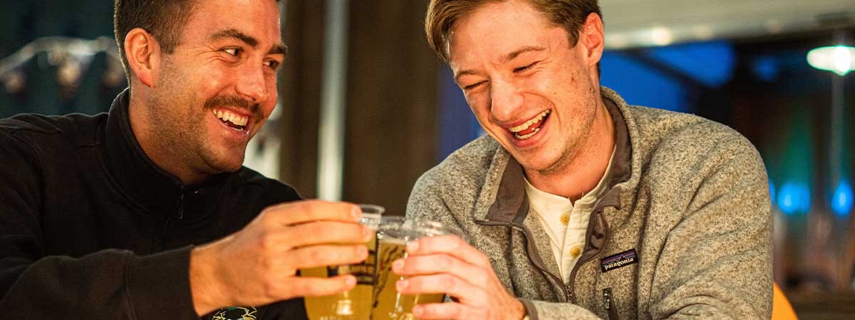 Zwei Männer sitzen bei einem Date an einem romantischen Lagerfeuer. Sie stoßen mit einem Getränk an.