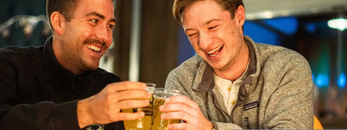 Zwei Männer sitzen bei einem Date an einem romantischen Lagerfeuer. Sie stoßen mit einem Getränk an.