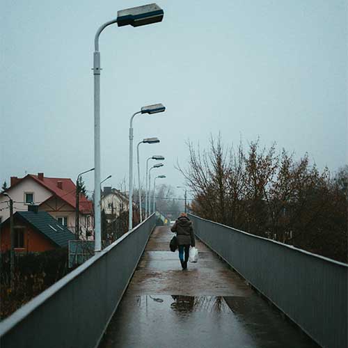 Ein düsteres, negativ geprägtes Bild einer regennassen Brücke, über die eine dunkel gekleidete Person läuft.