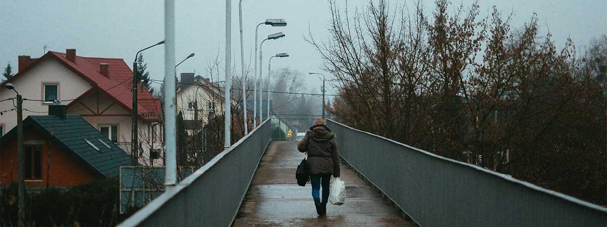 Ein düsteres, negativ geprägtes Bild einer regennassen Brücke, über die eine dunkel gekleidete Person läuft.