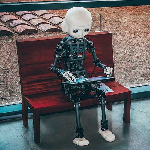 Ein Roboter mit Künstlicher Intelligenz sitzt auf einer Bank und liest Texte in einem Magazin.