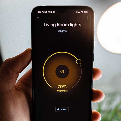 Ein Smartphone mit einer Smart-Home-App, die die Lichter der Wohnung steuert. Auf dem Display steht: Living Room lights, 2 lights, 70% Brightness, color.