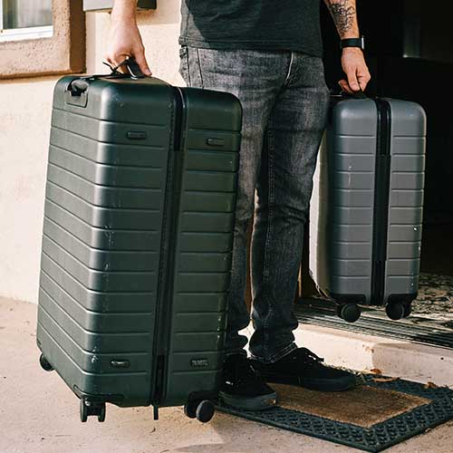 Ein Mann steht vor der Tür seiner Wohnung und trägt zwei gepackte Koffer heraus.