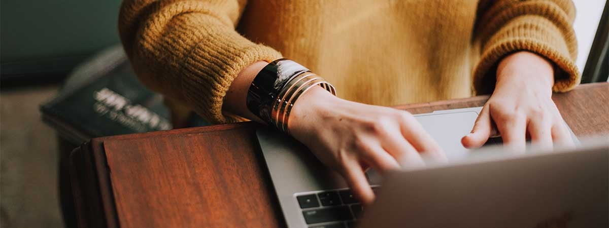 Eine Frau mit gelbem Pulli schreibt auf der Tastatur eines Laptops. 