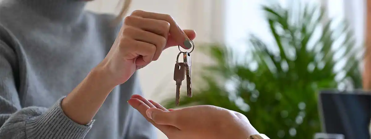 Eine junge Frau übergibt einer anderen Frau einen Wohnungsschlüssel. 