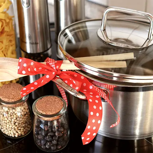 Foto von einem Kochfeld mit einem Kochtopf, Kochlöffeln und Vorratsgläsern, die mit Gewürzen und Nudeln gefüllt sind.