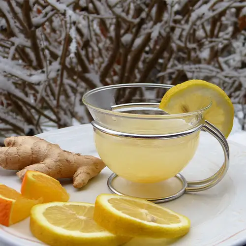 Teller mit Zitronen, Ingwer und einer Tasse mit Tee vor einem verschneiten Hintergrund.