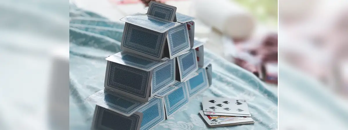 Ein Haus aus Spielkarten auf einer hellblauen Tischdecke. 