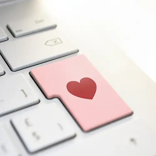 Foto vom Ausschnitt einer weißen Laptoptastatur mit einer rosa Entertaste, auf der ein rotes Herz abgebildet ist.