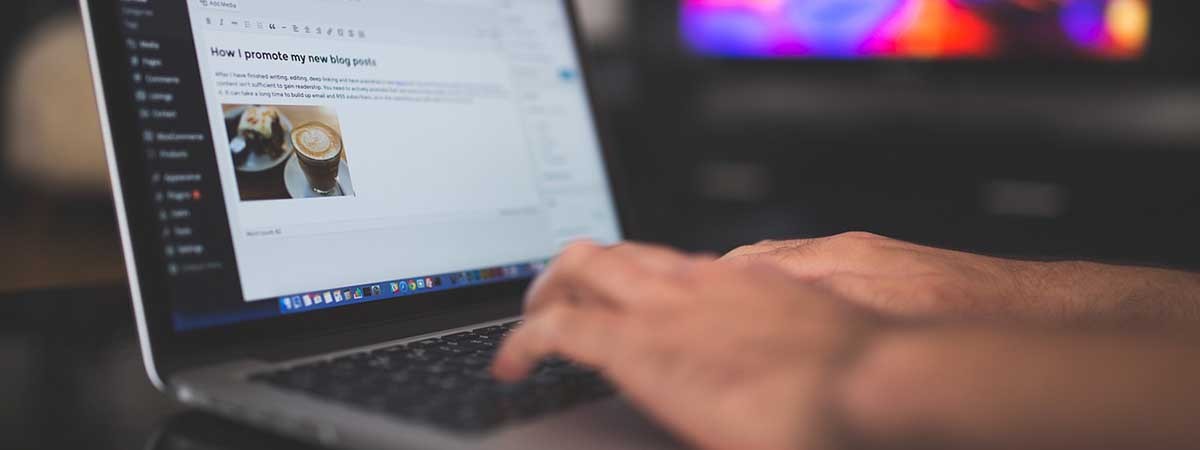 Ein Foto einer Person, die an einem Blogbeitrag auf einem Laptop arbeitet, während im Hintergrund ein bunter, verschwommener Bildschirm zu sehen ist. 