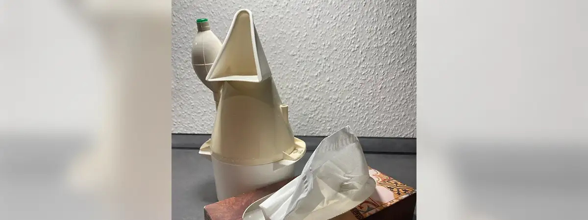 Ein Inhalator und eine Box mit Taschentüchern auf einer dunklen Oberfläche vor einer weißen Wand.