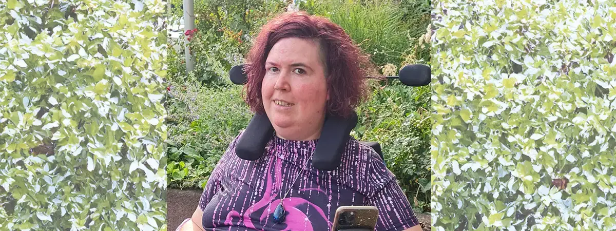 Ein Foto von Jasmin in ihrem elektrischen Rollstuhl. Sie trägt ein lilafarbenes T-Shirt und lächelt in die Kamera.