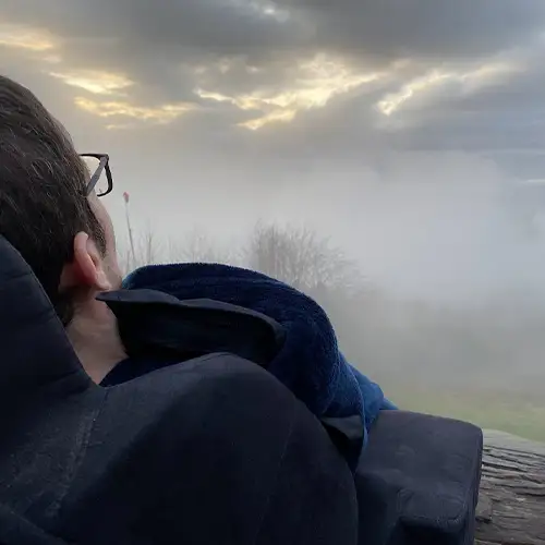 Ein Bild von Roberto, der im Rollstuhl in eine neblige Landschaft mit dunklen Wolken am Himmel blickt.