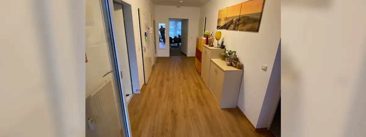 Ein Foto von Robertos barrierefreiem Flur mit Holzoptik-Boden, modernen Möbeln und Landschaftsbildern an der Wand, der zu mehreren Räumen führt.