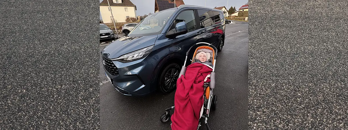 Ein Foto von Carolin, die sich draußen auf der Straße vor ihrem behindertengerechten Auto befindet und durch eine Decke gewärmt wird.