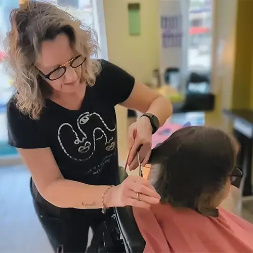 Camilla sitzt in einem Friseurstuhl und lässt sich von einer Frau die Haare schneiden. 
