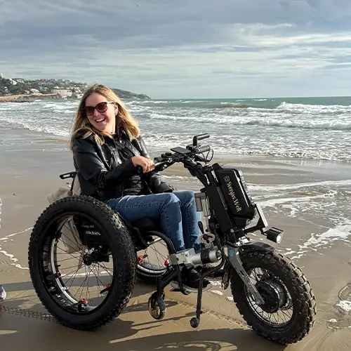 Ein Foto von Svenja auf einem elektrischen Rollstuhl-Zuggerät am Strand.
