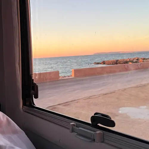 Ein Foto, das den Blick aus dem Wohnmobil auf einen Sonnenaufgang am Meer zeigt.