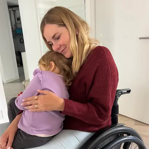 Svenja sitzt im Rollstuhl und hat ihre Tochter auf dem Schoß, welche sich an sie kuschelt