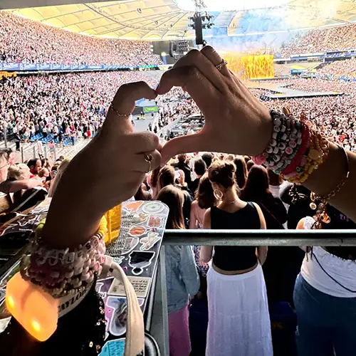 Ein Foto von Vanessa und ihrer Begleitung, die gemeinsam ein Herz mit ihren Händen formen, während sich im Hintergrund viele Konzertbesucher befinden.
