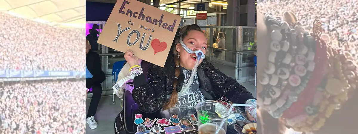 Ein Foto von Vanessa, die in ihrem mit Aufklebern verzierten Rollstuhl sitzt, ein glitzerndes Outfit trägt und ein Plakat mit der Aufschrift „Enchanted to meet you“ hochhält. 