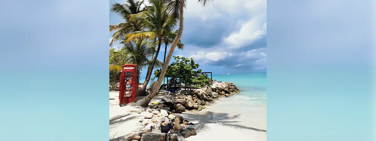 Ein weißer Sandstrand mit türkisem Meer und Palmen sowie einer roten Telefonzelle.