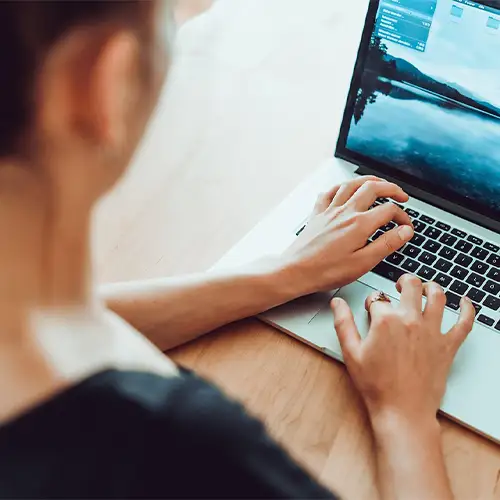 Ein Foto einer Frau, die an ihrem Schreibtisch sitzt und an ihrem Laptop arbeitet.