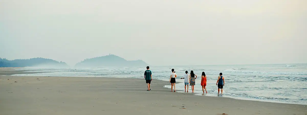 Eine Gruppe junger Menschen spaziert am Strand entlang und genießt den Blick aufs Meer.