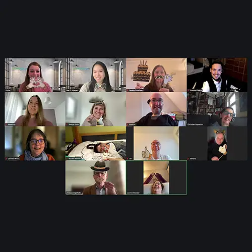 Foto des virtuellen Meetings: Redaktionsteam und admedicum halten lächelnd Fotorequisiten in die Kamera.