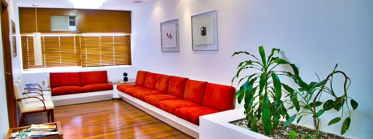 Ein Wartebereich einer Arztpraxis mit roten Sitzbänken, Holzboden, Pflanzen und Zeitschriften.