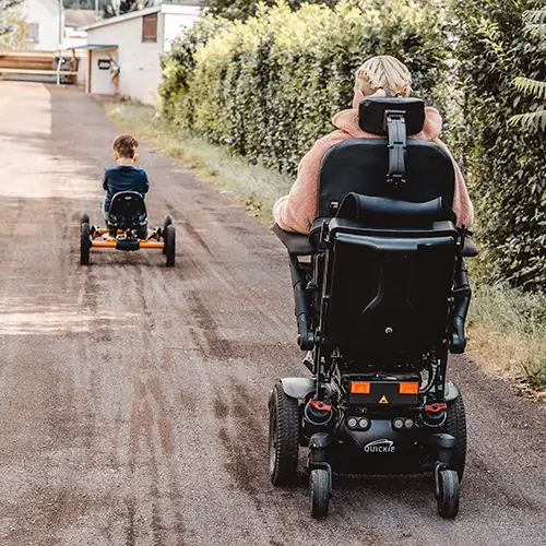 Alina im Elektrorollstuhl mit ihrem Kind, die gemeinsam eine ruhige Straße entlangfahren.