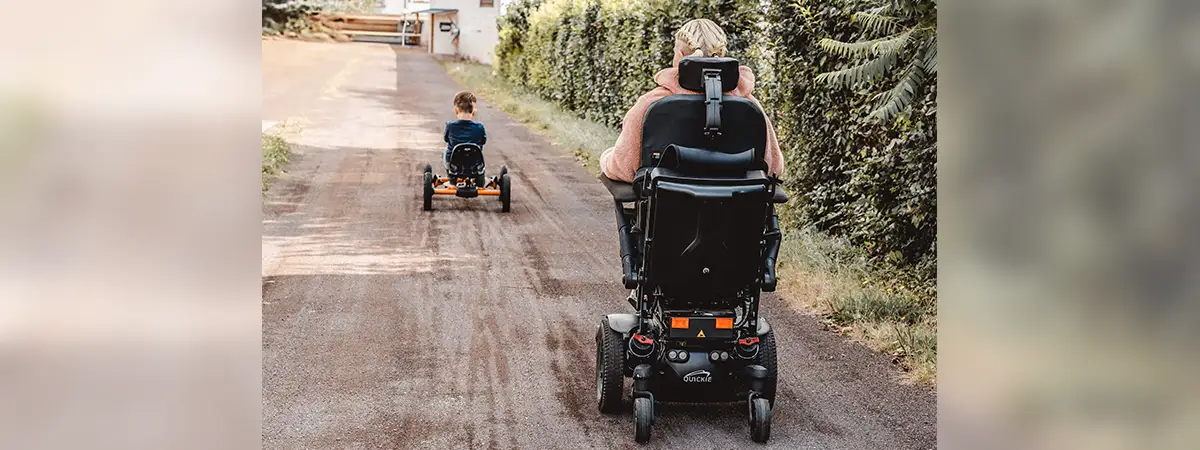 Alina im Elektrorollstuhl mit ihrem Kind, die gemeinsam eine ruhige Straße entlangfahren.