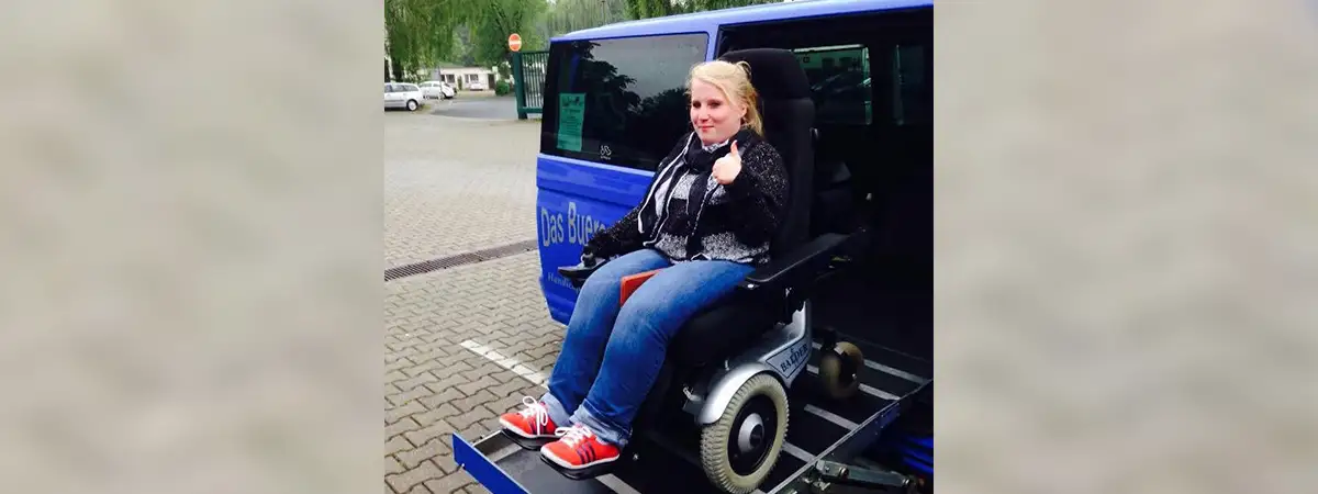 Ein Foto von Sandra, die in einem Elektrorollstuhl auf der Hebebühne ihres Autos sitzt.