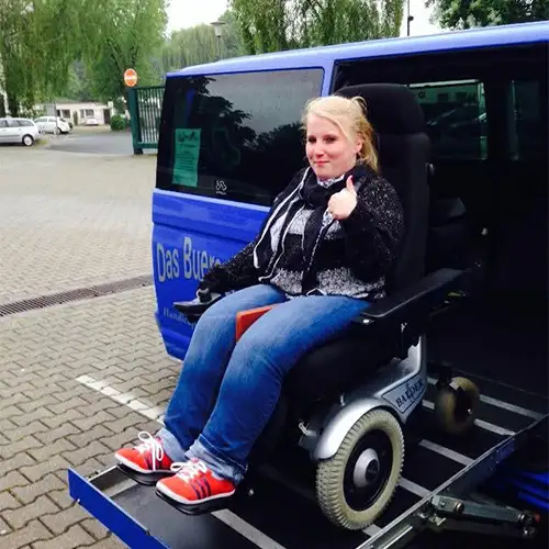 Ein Foto von Sandra, die in einem Elektrorollstuhl auf der Hebebühne ihres Autos sitzt.