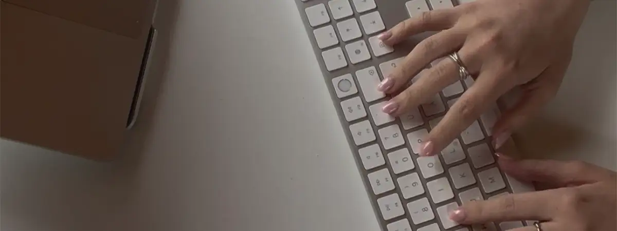 Ein Foto von oben von Amelies Händen beim Tippen auf einer Tastatur neben ihrem Laptop.