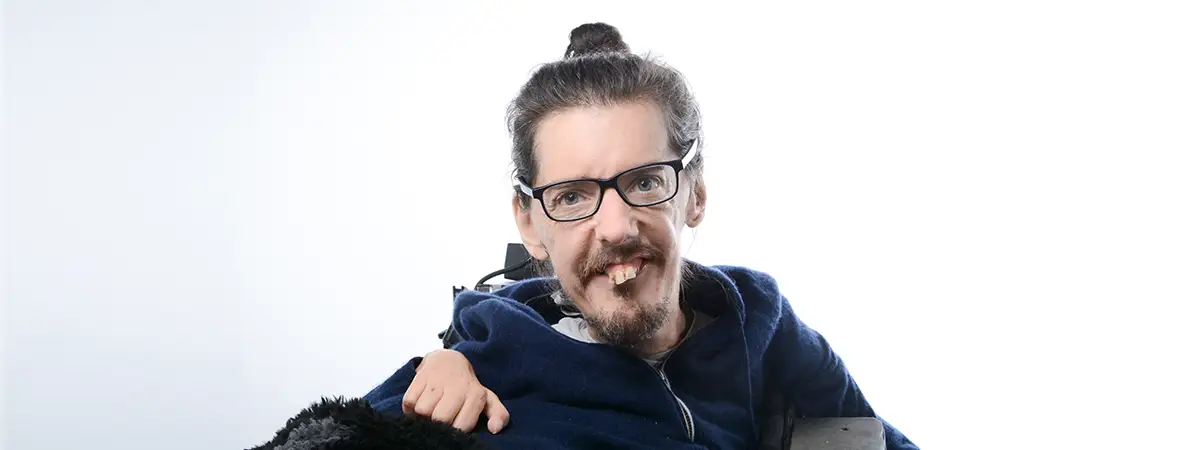 Christian sitzt im Elektrorollstuhl und blickt freundlich in die Kamera.