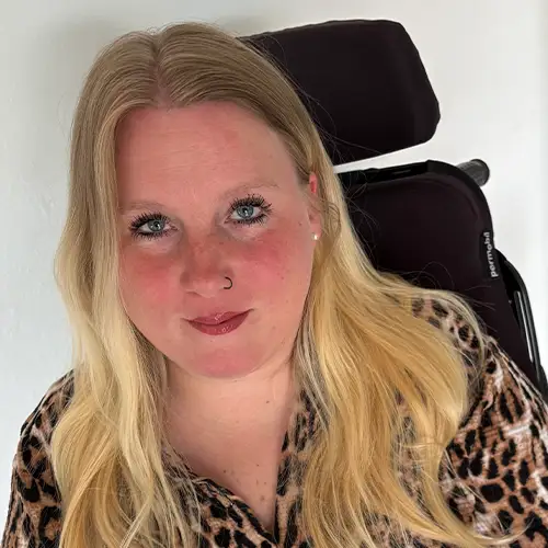 Sandra sitzt in einem Elektrorollstuhl und blickt freundlich in die Kamera.