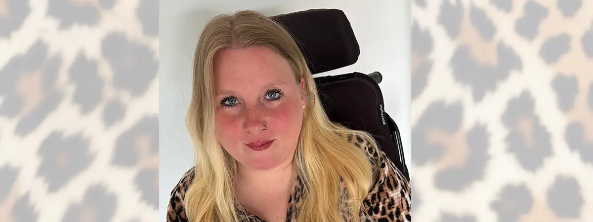Sandra sitzt in einem Elektrorollstuhl und blickt freundlich in die Kamera.