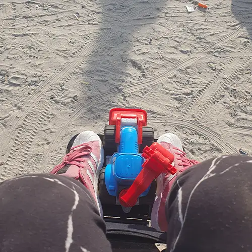 Alina fährt im Elektrorollstuhl, zwischen ihren Füßen liegt Sandspielzeug.