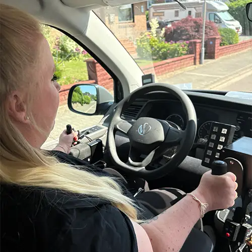 Sandra sitzt in ihrem umgebauten Fahrzeug und hält den Joystick zur Steuerung in der Hand.
