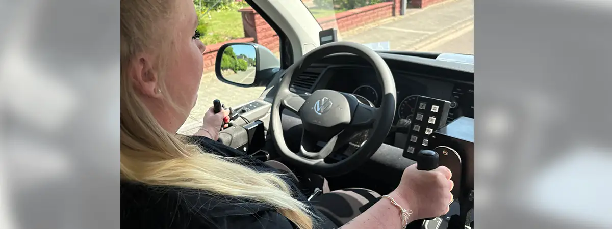Sandra sitzt in ihrem umgebauten Fahrzeug und hält den Joystick zur Steuerung in der Hand.