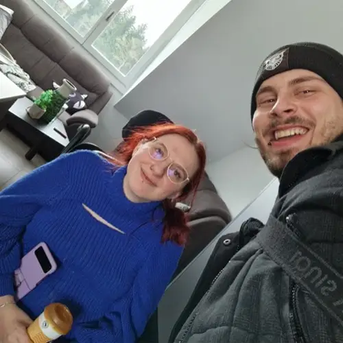 Lys und ihr Ehemann stehen in einer Wohnung und blicken freundlich in die Kamera
