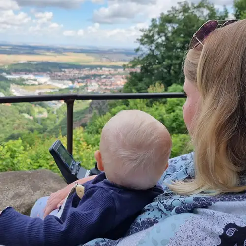 Sandra sitzt im E-Rolli mit Baby auf dem Schoß auf einem Hügel und schaut in die Ferne