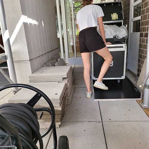Eine Frau schiebt Phil’s verpackten Rollstuhl in ein Gebäude