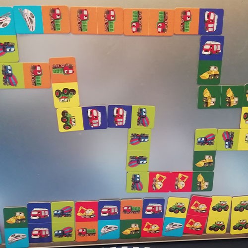 Bunte magnetische Kinder-Dominokarten mit Fahrzeugmotiven hängen an einer silbernen Tafel.