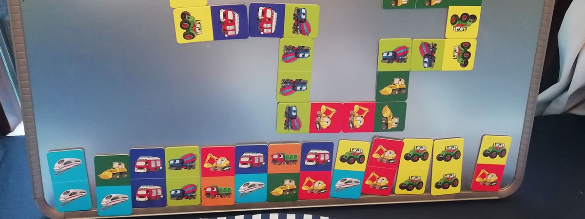 Bunte magnetische Kinder-Dominokarten mit Fahrzeugmotiven hängen an einer silbernen Tafel.