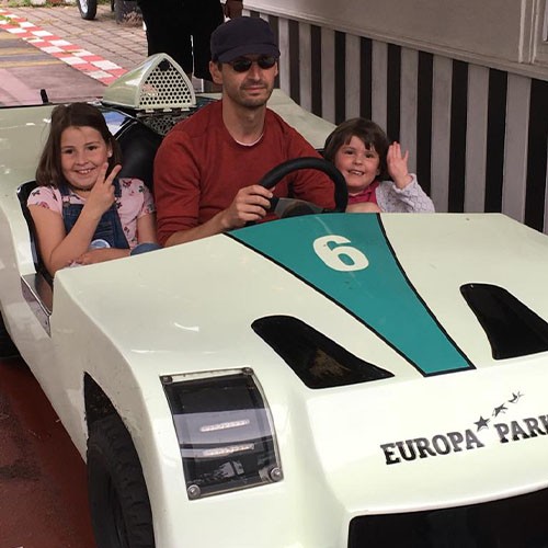 Ein Vater sitzt mit seinem beiden Töchtern in einem Fahrgeschäft in einem Freizeitpark