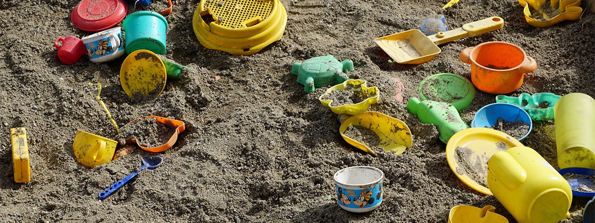 In einem Sandkasten für Kinder liegen bunte Sandspielzeuge wie Schaufeln, Förmchen und ein Sieb.